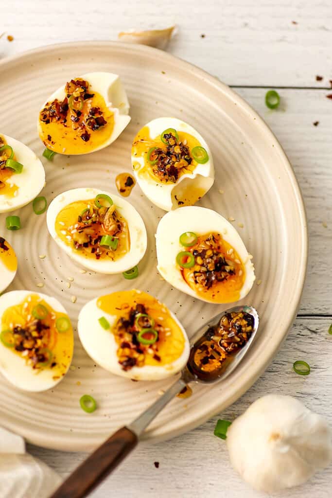 Garlic chili oil drizzled over hard boiled eggs on white plate.
