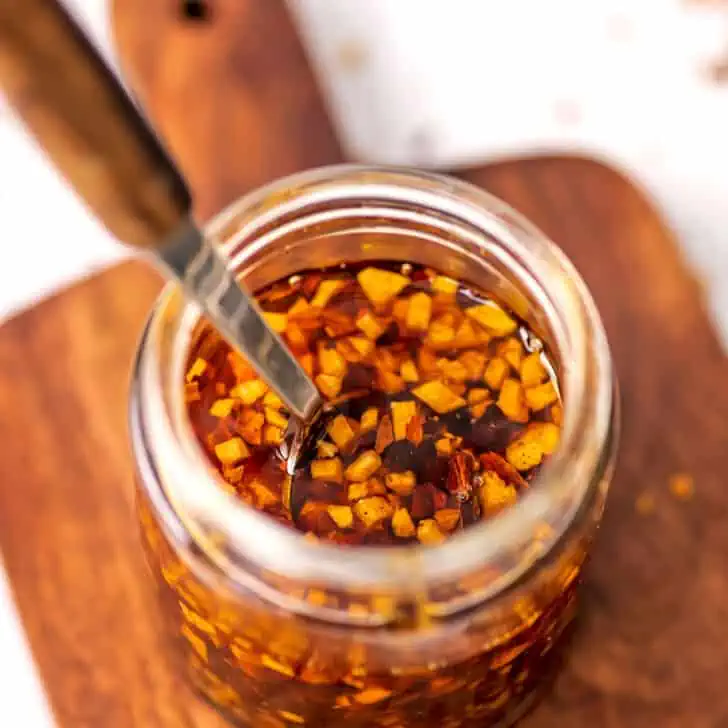 Wooden handle spoon resting in jar of garlic chili oil.