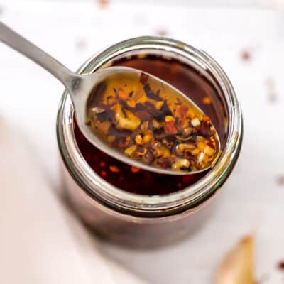 Chili garlic oil in a glass jar, spoonful of oil over the jar.