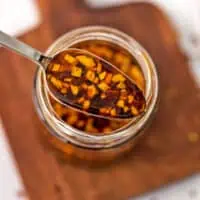 Spoonful of crunchy garlic chili oil over a glass jar.