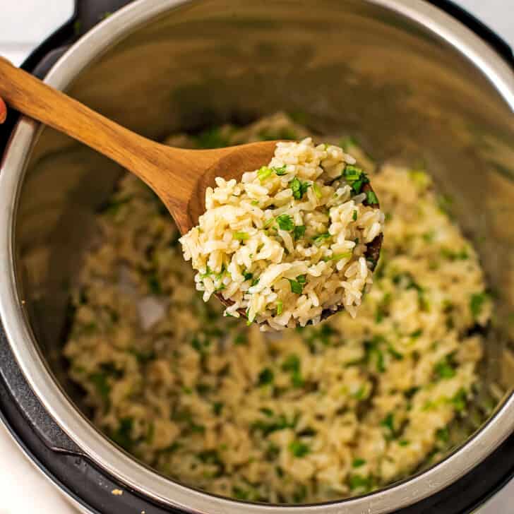 Large wooden spoon full of cilantro lime brown rice over instant pot.