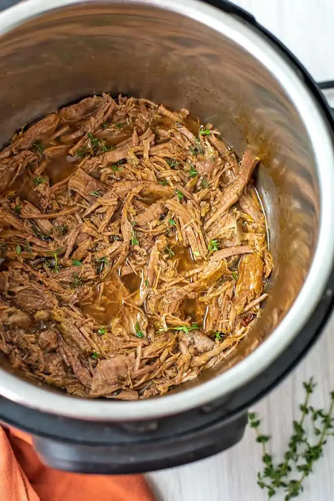 Instant pot full of pulled beef, thyme leaves on the side.