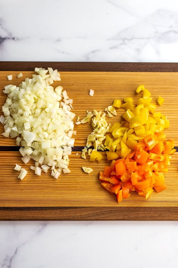 Chopped onion, sliced garlic and chopped bell peppers on wood cutting board.