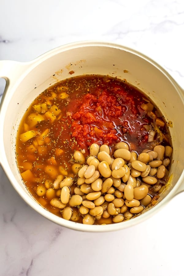 Butter beans and diced tomatoes to the rest of the stew ingredients in a pot.