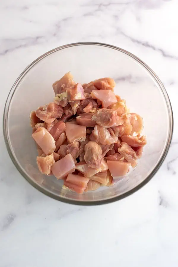 Chicken thighs cut into cubes in glass bowl.
