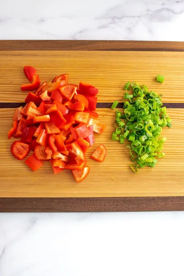 Chopped red bell peppers and green onions on wood cutting board.