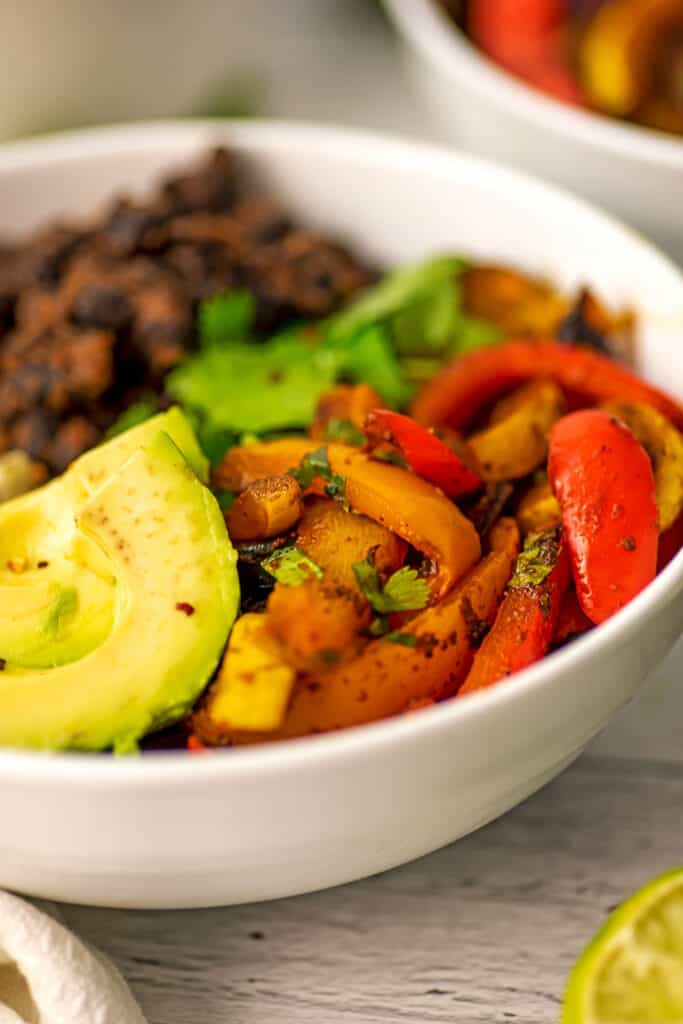 Fajita vegetables, avocado and black beans in a large white bowl.