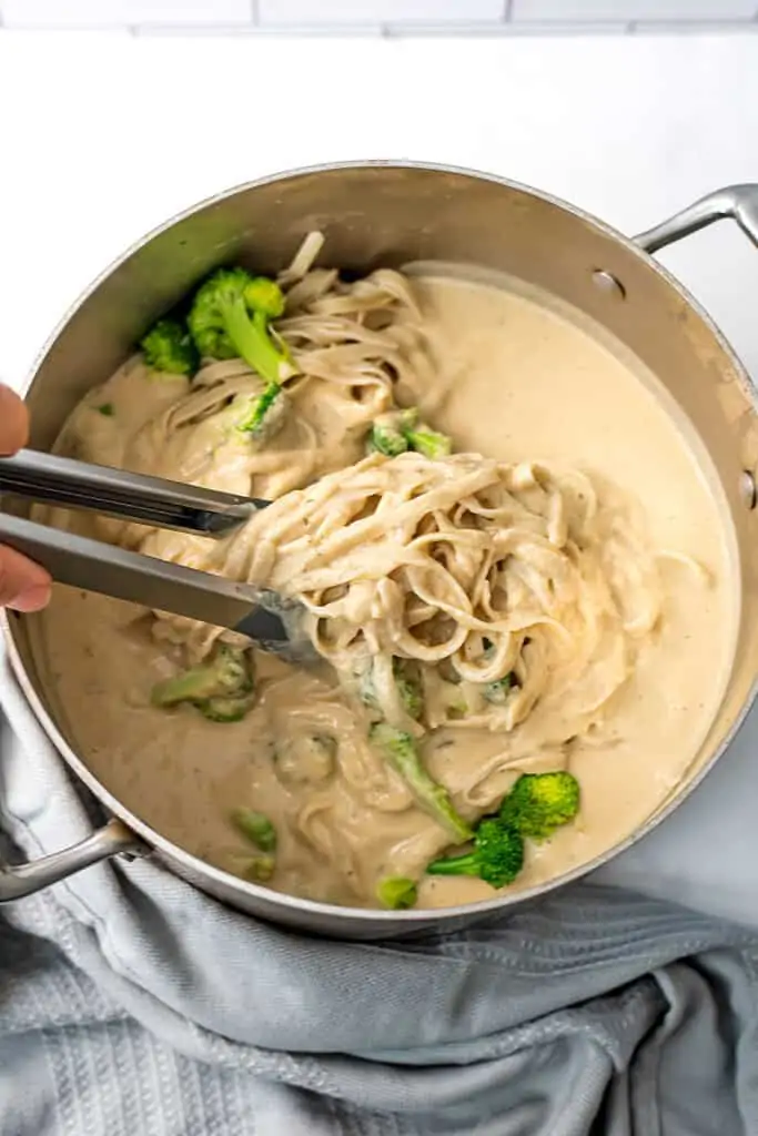 Silver tongs stirring white bean pasta sauce with fettucine pasta.