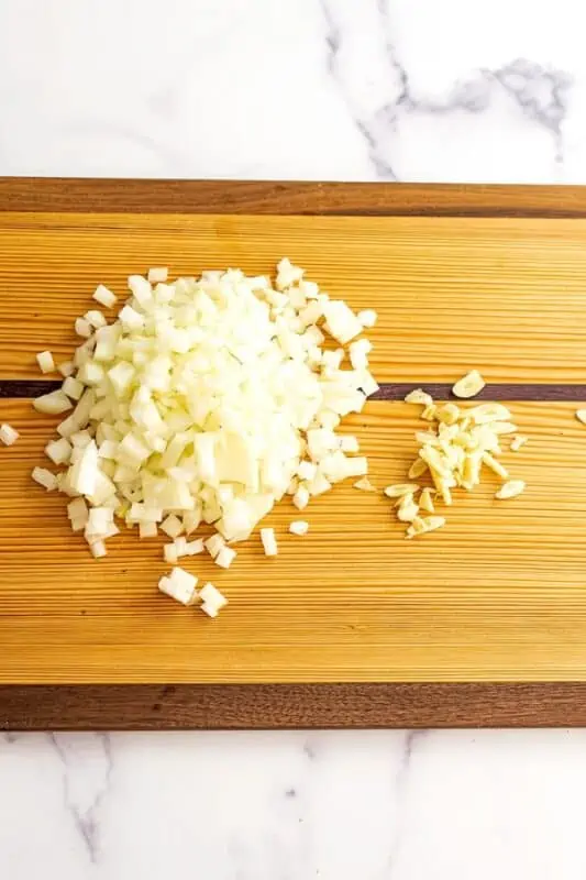 Chopped onion and sliced garlic on a wooden cutting board.
