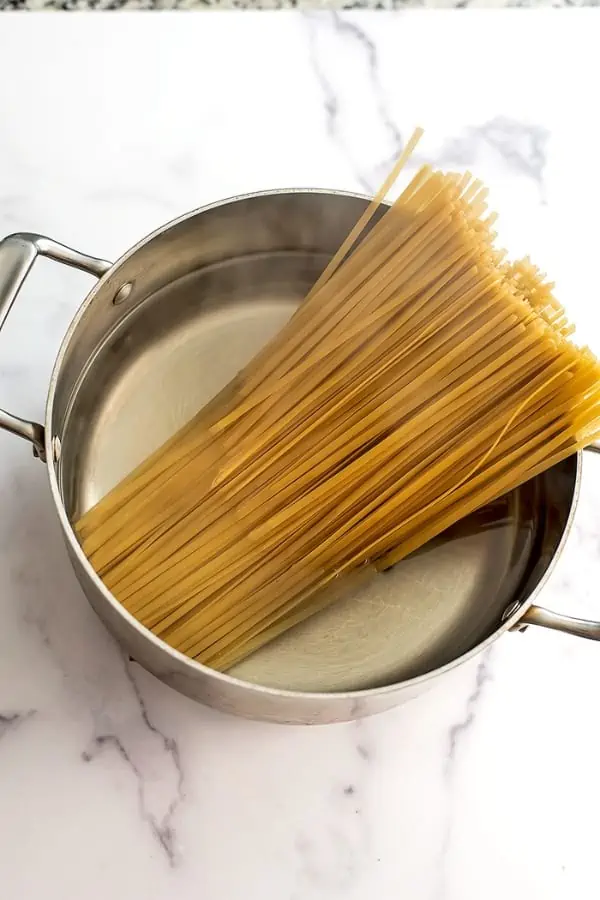 Dry fettucine noodles added to pot full of boiling water.