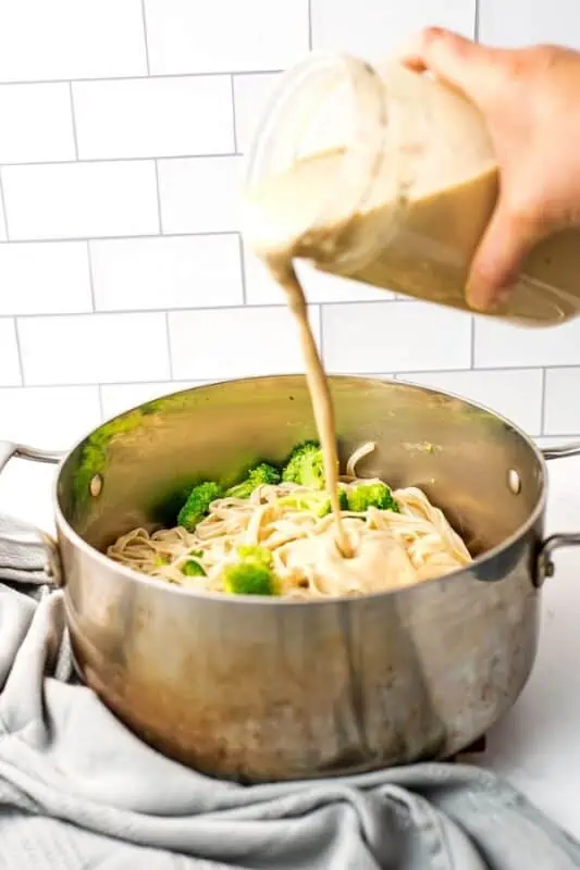 Vegan white bean alfredo sauce being poured over fettucine and broccoli.