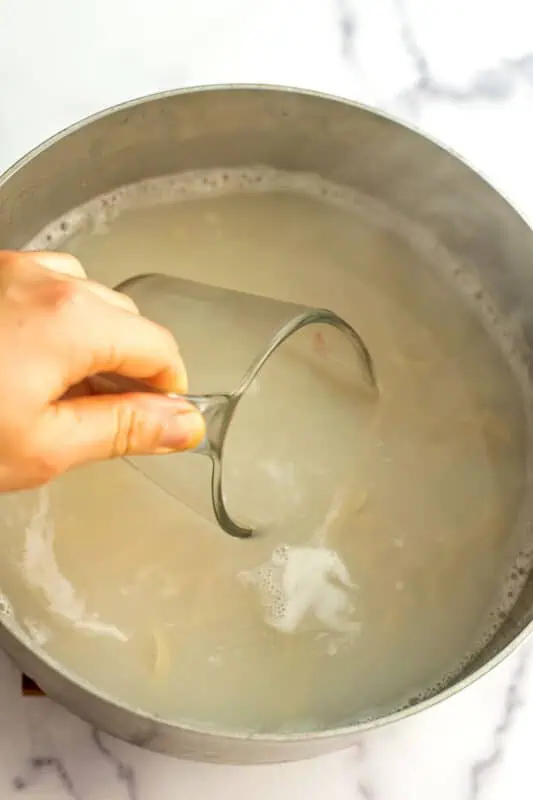Glass measuring cup being dipped into pot with pasta water.