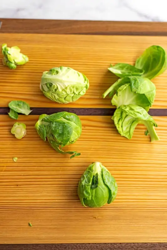 Brussel sprouts on wood cutting board, with stems being removed.