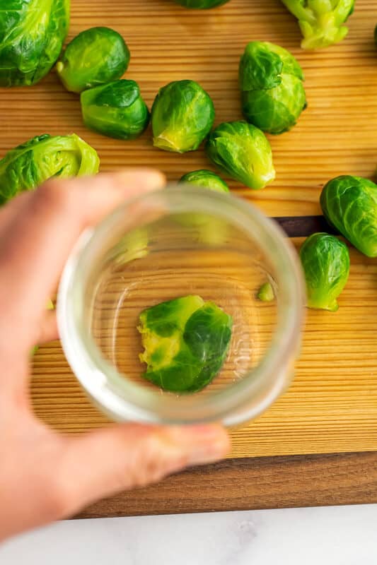 Glass smashing brussel sprout on wood cutting board.