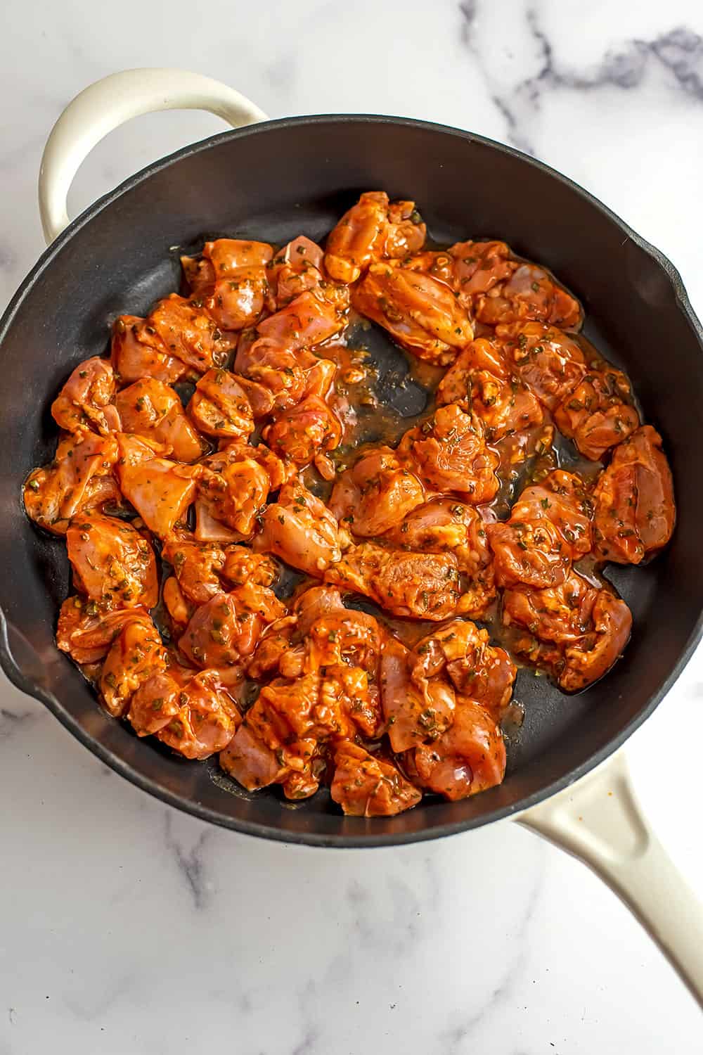 Buffalo sauce over raw chicken bites in cast iron skillet.