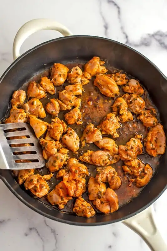 Silver spatula moving chicken around in cast iron skillet.