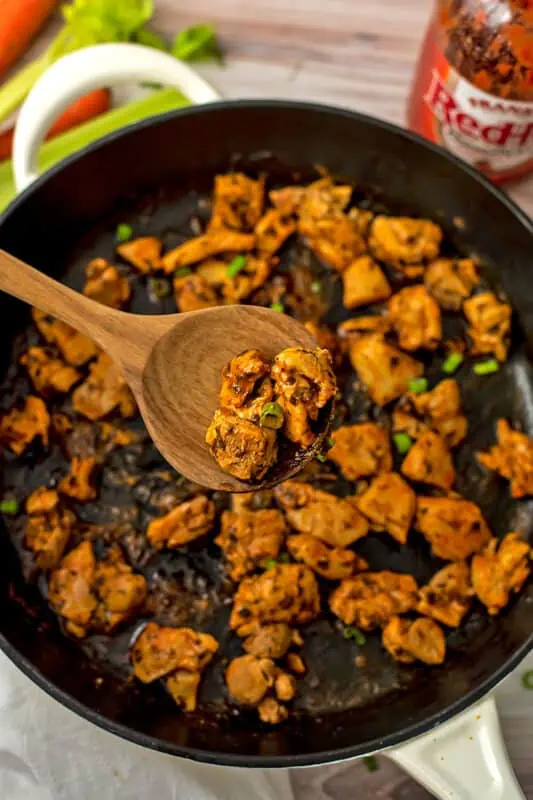 Skillet of buffalo chicken, wooden spoon picking up the chicken.