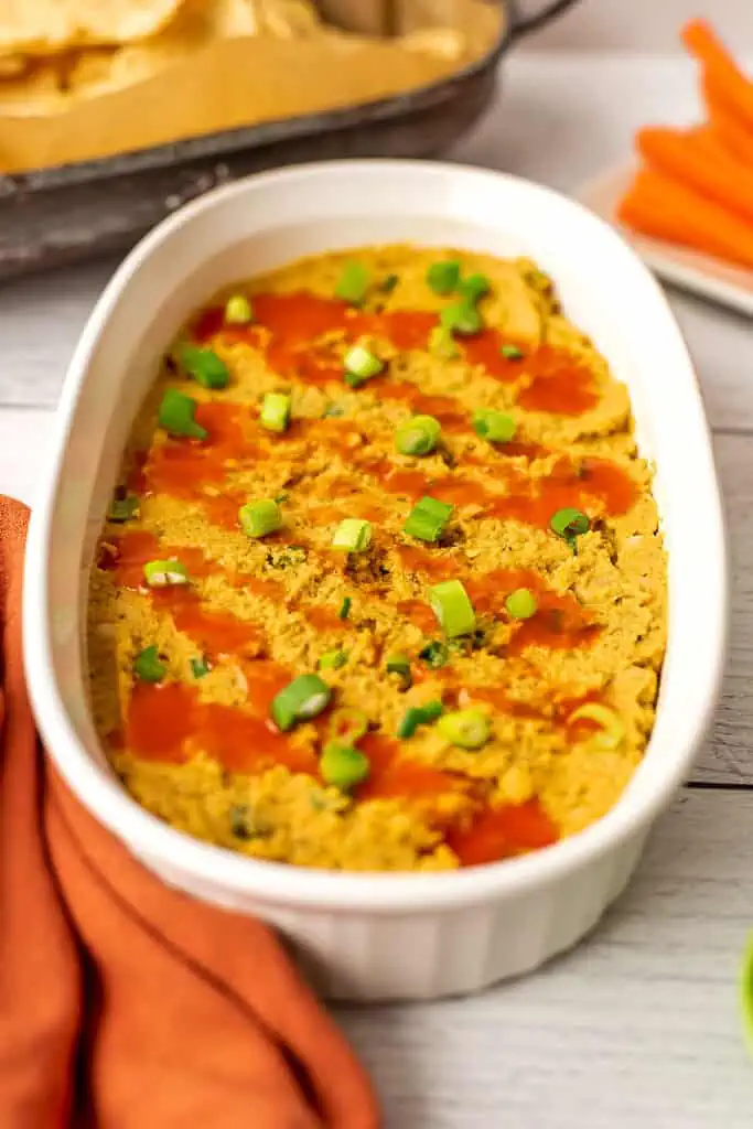 Chickpea buffalo dip in a white casserole dish with orange napkin on the side.