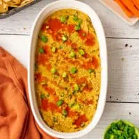 Buffalo chickpea dip in a oval casserole dish, with hot sauce on top.