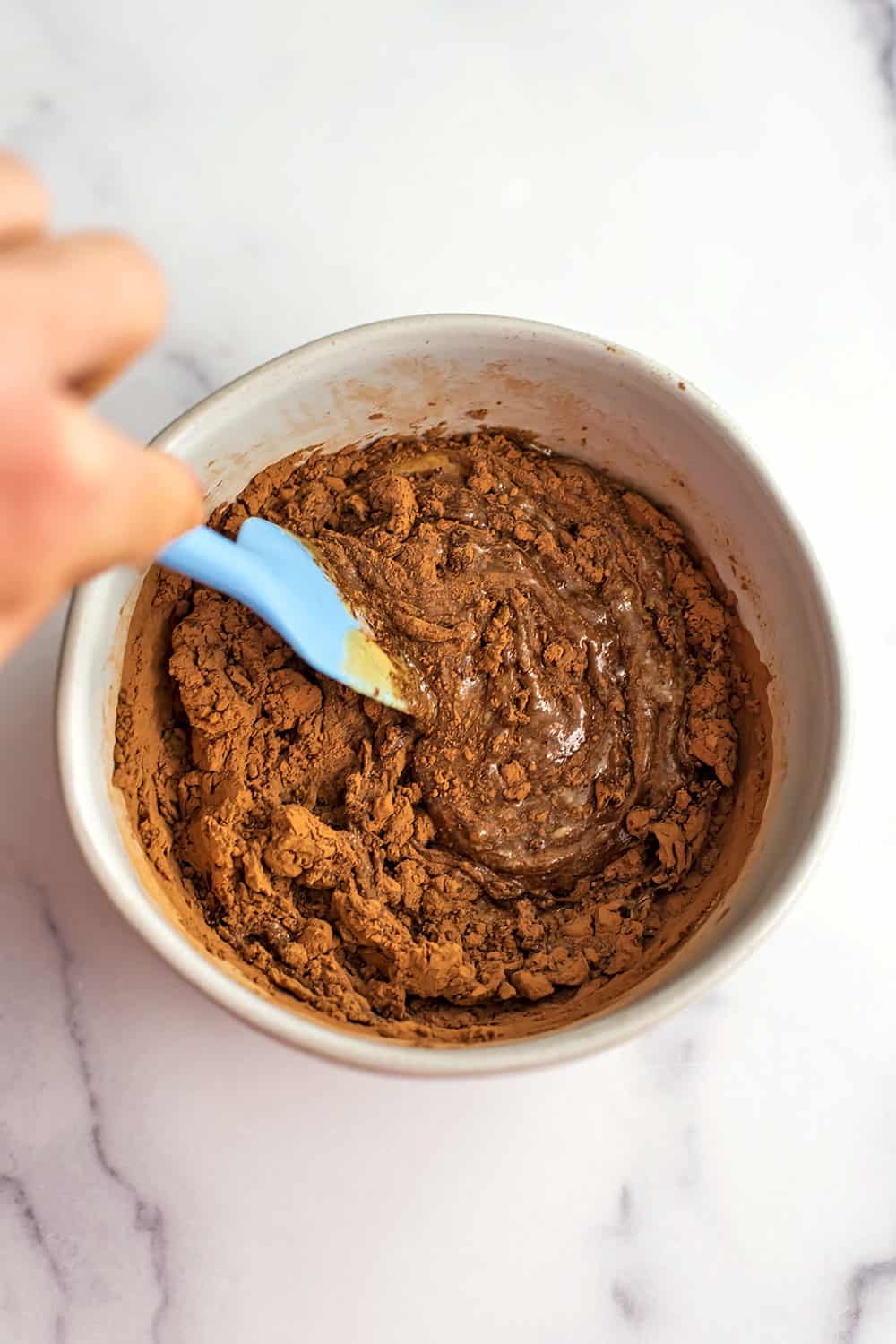 Blue spatula stirring cacao powder in with tahini.