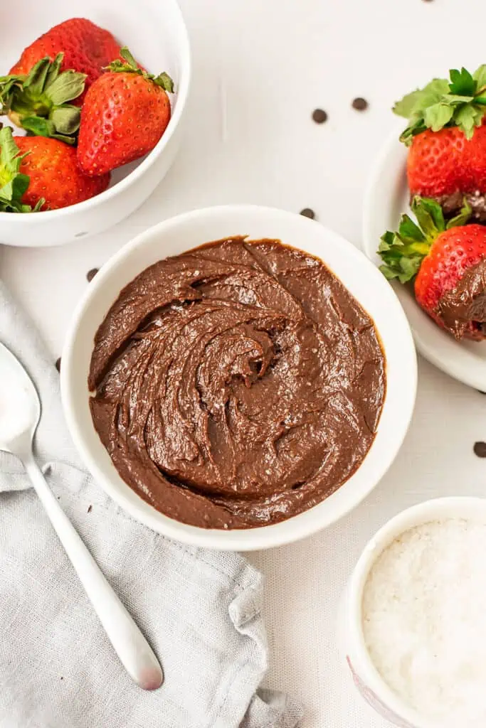Bowl of chocolate tahini spread with strawberries in a bowl behind them.