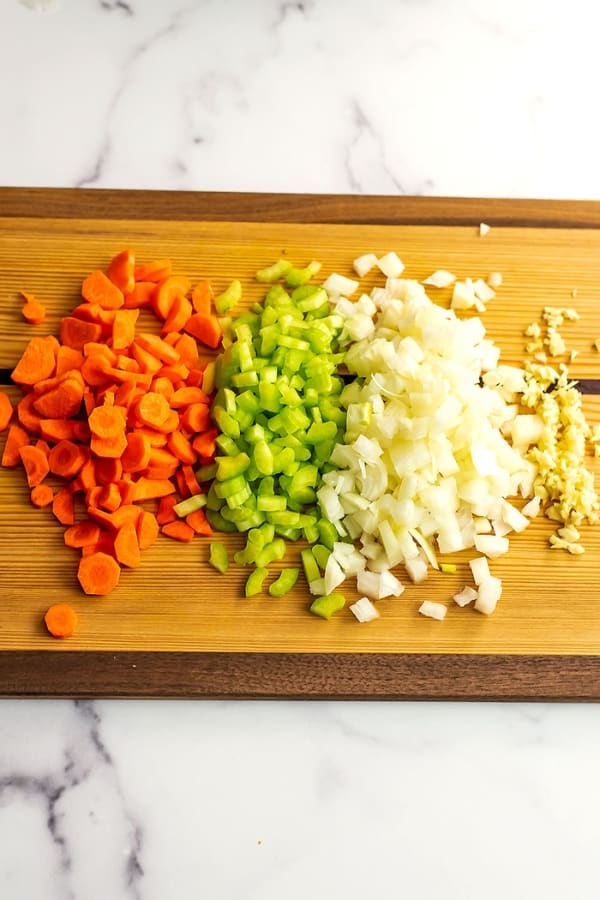 Finely chopped carrots, celery, onion and garlic on a wood cutting board.