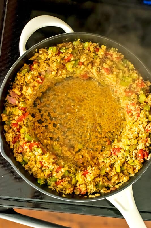 Dirty cauliflower rice pushed to edges of skillet, water boiling in center.. 
