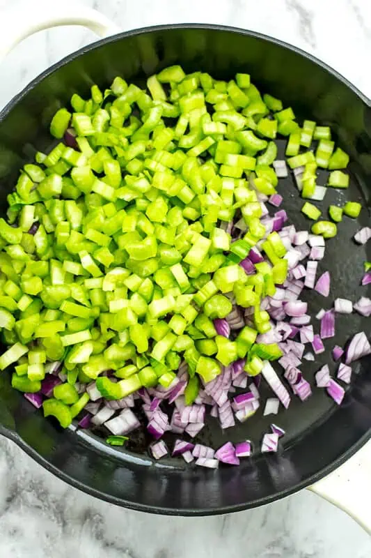 Cast iron skillet filled with chopped celery and red onion. 