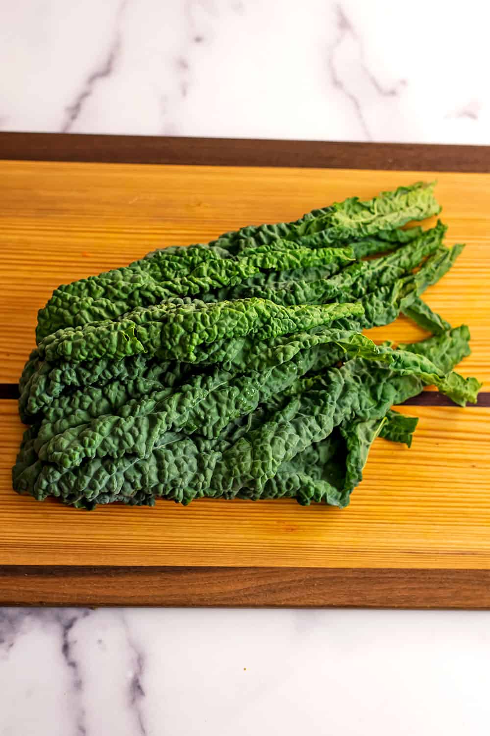 Kale leaves with the stems removed on a wood cutting board.