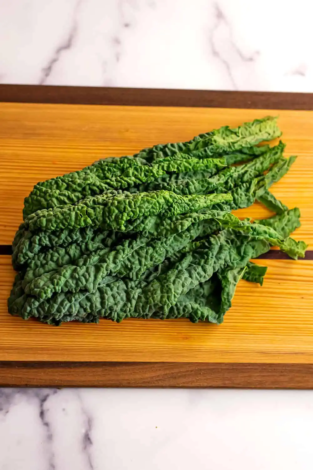 Kale leaves with the stems removed on a wood cutting board.