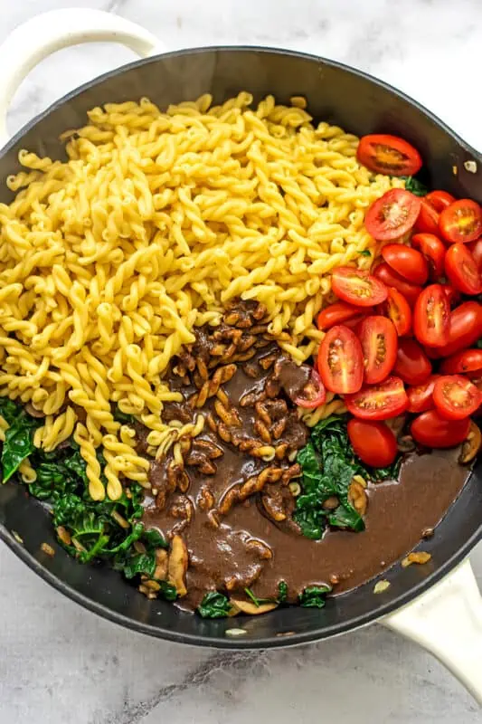 Large skillet filled with pasta, tomatoes, balsamic sauce, and kale.