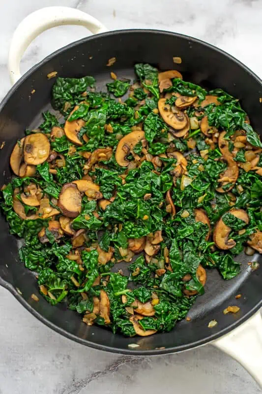 Wilted kale and mushrooms in a large skillet.