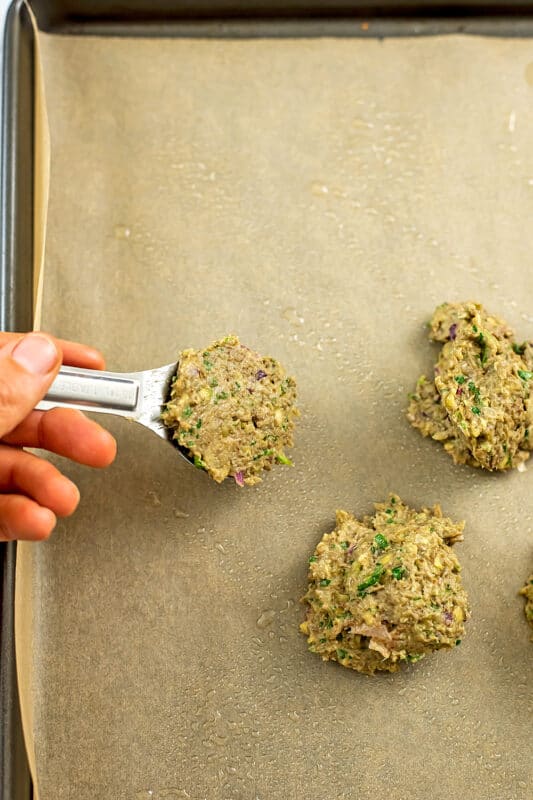 Tablespoon full of lentil falafel mixture over baking sheet.