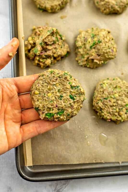 Hand holding a formed lentil falafel over baking sheet.
