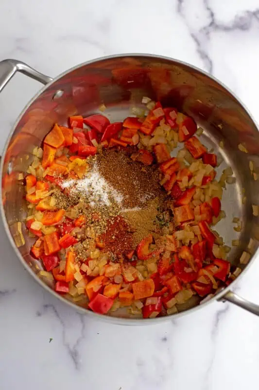 Spices added to onions and bell peppers in pot.
