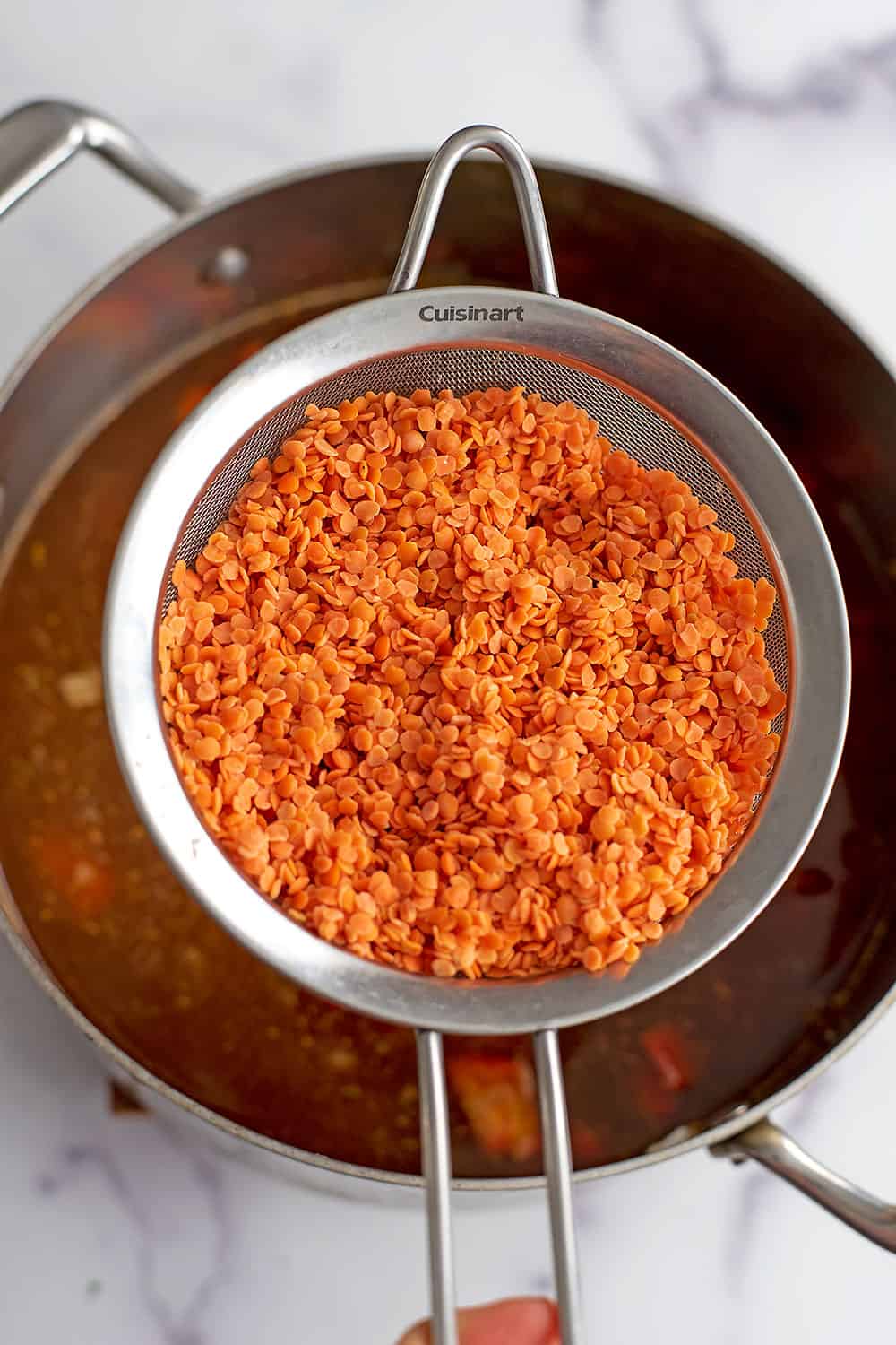 Rinsed red lentils in a mesh strainer over soup.