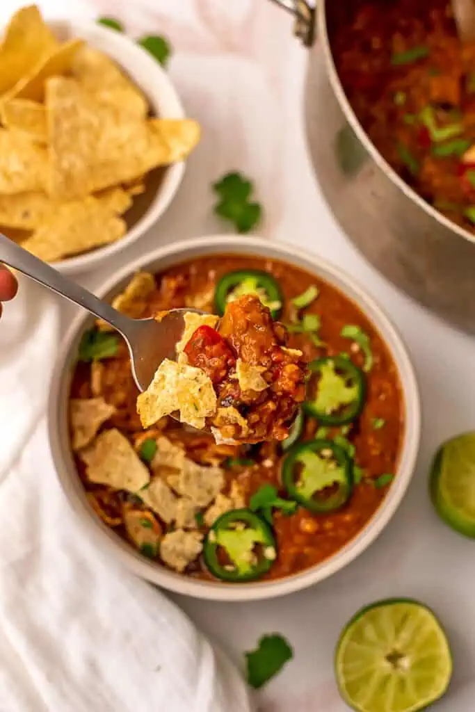 Lentil tortilla soup in a white bowl with bowl of tortilla chips in background.