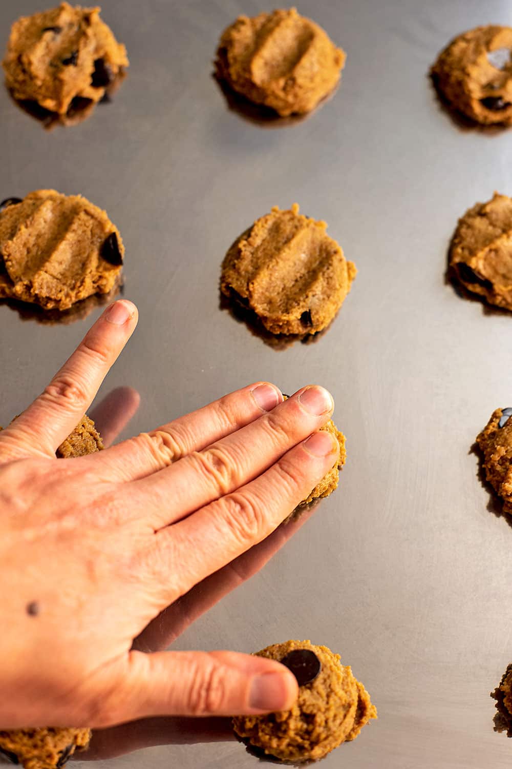 Hand pressing down cookie dough on baking sheet.