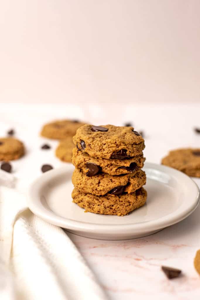 Four chocolate chip oat flour cookies stacked on a white plate.