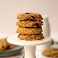 Four oat flour chocolate chip cookies on a small white cookie stand.