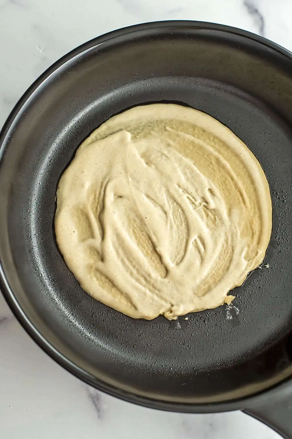 Oat flour tortilla in black skillet before flipping.
