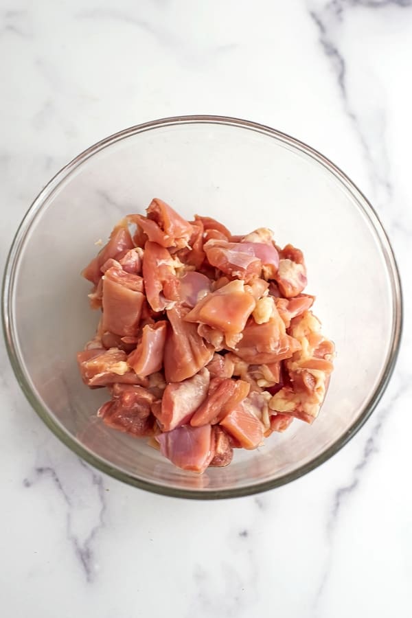 Raw chicken cubes in glass bowl.