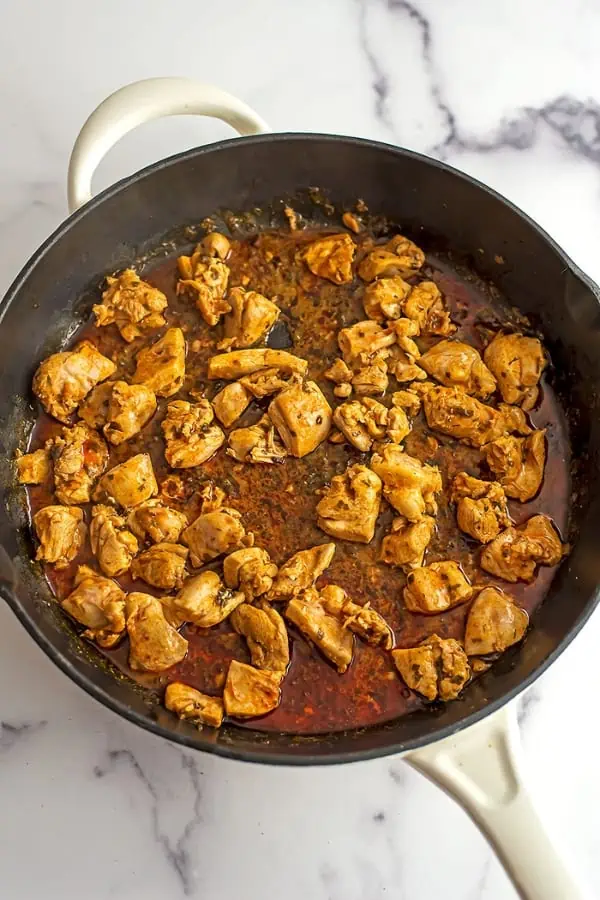 Chicken cubes in cast iron skillet with buffalo sauce.