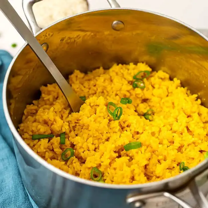 Turmeric garlic rice in pot with large spoon in the pot.