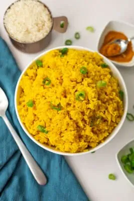 White bowl filled with turmeric garlic rice with blue napkin on the side.