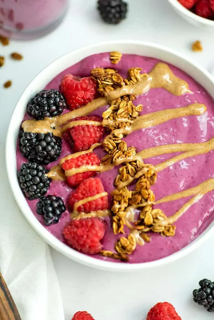 Blackberry raspberry smoothie bowl with blackberry and raspberry fruit on top. Also as toppings granola and almond butter drizzle.