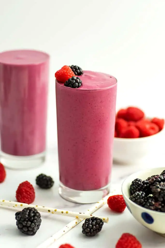 A blackberry raspberry smoothie filled high in a tall class with raspberry and blackberries on topping the smoothie.  