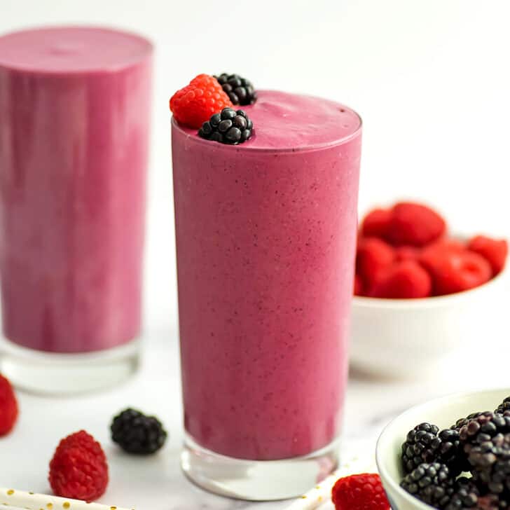 A blackberry raspberry smoothie filled high in a tall class with raspberry and blackberries on topping the smoothie.