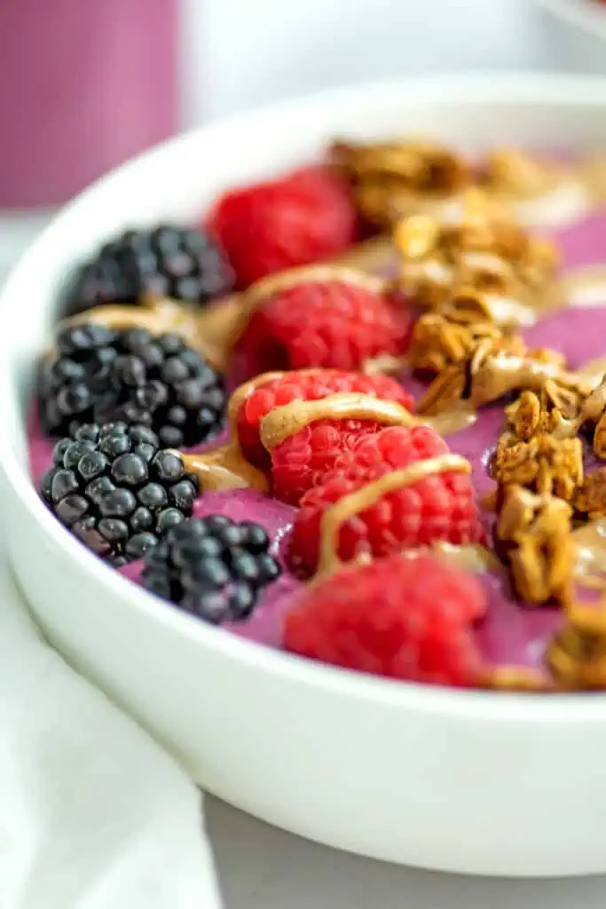 An up close view of a blackberry raspberry smoothie bowl with blackberries, raspberries, granola and almond butter drizzled on top.
