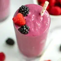 Blackberry raspberry smoothie topped with blackberries and strawberries with a straw.